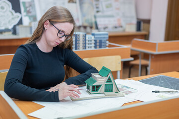 Caucasian young woman making a model of a building. Student of the construction university. 