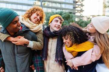 Young group of multiracial friends in warm clothes having fun on winter outside. Diverse teenage Gen Z students hanging out and laughing while enjoying free day at city street. Friendship concept