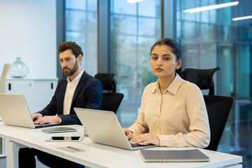 Focused businesswoman working on laptop in modern office with colleague