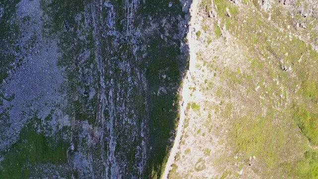 Aerial view of a rugged mountain ridge from above displaying a stark contrast of dark rocks and vibrant green vegetation, Bruck an der Gro&szlig;glocknerstra&szlig;e, Salzburg, Austria.
