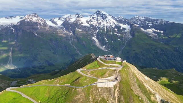 Aerial view of the winding Gro&szlig;glockner High Alpine Road leading to the mountain peak, contrasting green slopes with snow-capped mountains, Bruck an der Gro&szlig;glocknerstra&szlig;e, Austria.
