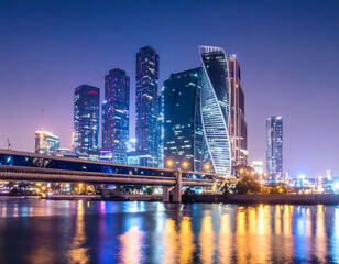 Fototapeta premium Modern city skyline at night reflecting on water with illuminated buildings and bridge