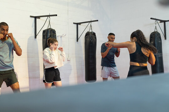 Hispanic instructor leading diverse students boxing at gym with heavy punching bags