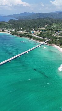 Vertical drone aerial of Tsunoshima Bridge over emerald blue ocean, coastal road in Japan, summer travel concept