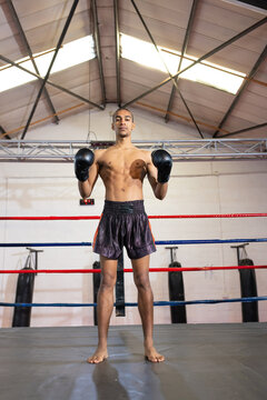 African american male boxer standing inside boxing ring in black gloves and orange shorts