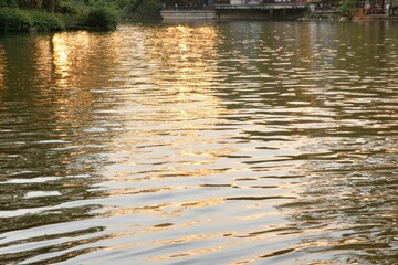 Golden reflections on rippled water, trees and a distant structure mirrored