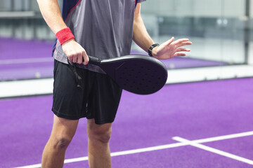 Male padel player in sportswear on purple court, gripping black racket and raising open hand
