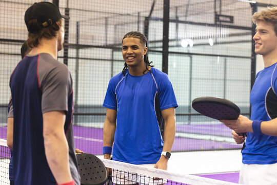 Diverse male friends in sportswear chatting and laughing on purple padel court holding rackets - Powered by Adobe