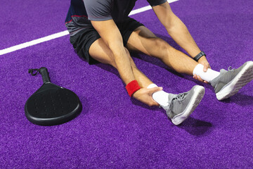 Athletic man stretching in sportswear on padel court with racket, red wristband, fitness tracker