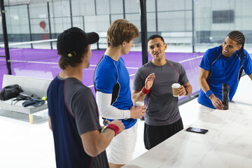 Diverse male teammates gathering around court-side counter with coffee cups and bottle
