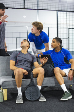 Diverse group of male athletes with coach coaching with paddle and tablet on padel court