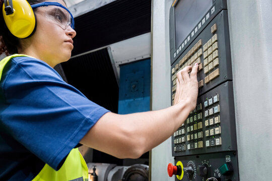 Maintenance engineer in protective workwear operating CNC machine keypad in modern factory
