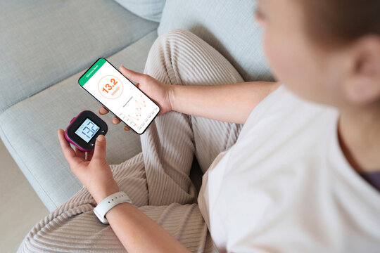 Woman checking blood sugar level through glucometer and smart phone at home