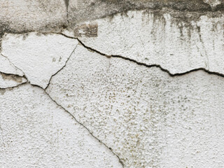 Textured view cracked and aged concrete surface. Large dark jagged crack that curves horizontally...