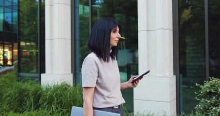 Young Caucasian businesswoman use smart phone with laptop on her business trip. Outdoors - Powered by Adobe