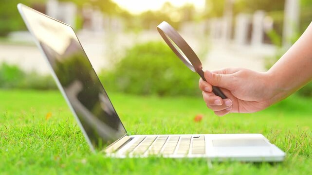 Examining a laptop with a magnifier in a green environment suggests digital investigation, precision, eco-conscious work, problem solving, and the pursuit of deeper understanding in modern tech life.
