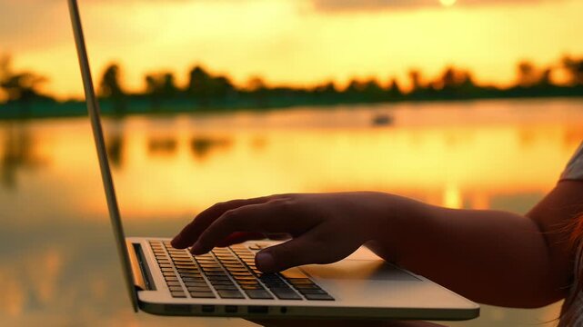 Using a laptop near the water as the sun sets highlights freedom, embracing remote work, mindful productivity, recharging in nature, and achieving a new blend of technology and tranquility.
