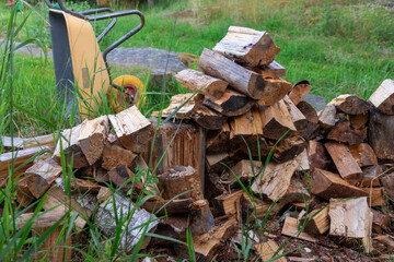Yellow garden wheelbarrow with sawn firewood near storage. Preparing renewable wood fuel for winter heating. Eco-friendly, sustainable rural lifestyle in Finland