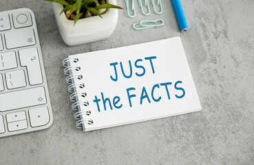 A white spiral notebook with blue writing that says Just the Facts