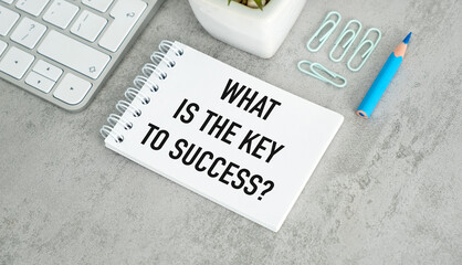 A white notebook with a blue pen on top of it. The notebook says What is the Key to Success
