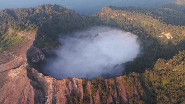 Aerial view of the Kelimutu volcano's crater lakes filled with ethereal clouds, surrounded by the lush green forest, Kelimutu, East Nusa Tenggara, Indonesia.