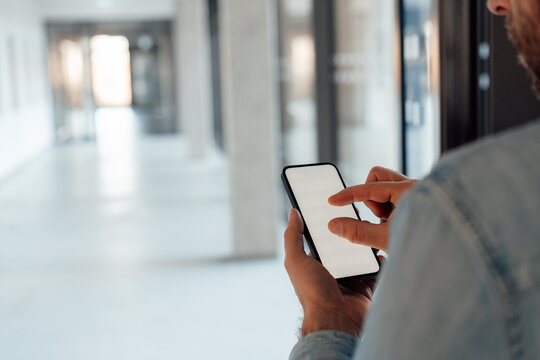 Businessman zooming screen of smart phone at corridor
