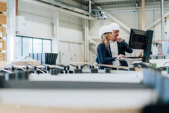 Businessman with hand on chin by colleague using desktop PC in factory