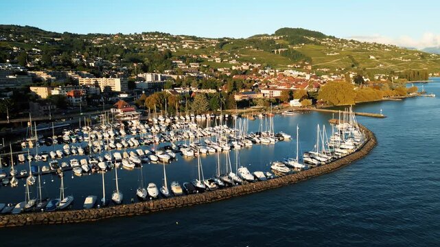 Aerial view of the Lutry harbor, filled with numerous boats, contrasting the deep blue water with the colorful town on the hillside, Lutry, Vaud, Switzerland.