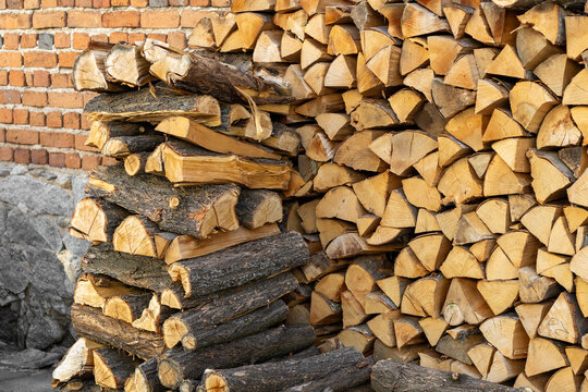 Neatly stacked pile of firewood rests against a brick wall, ready to provide warmth and comfort during the cold winter months. The varying textures of bark and split wood create a rustic aesthetic.