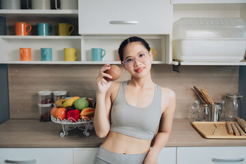 Young woman in gray sportswear holds a peach in a modern kitchen with colorful mugs and fresh fruits on display