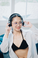 Naklejka premium Young woman enjoying music at home, wearing headphones, casual attire, relaxing in modern living space, lifestyle concept