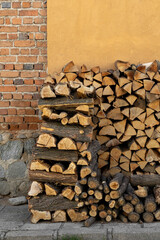 Firewood stacked against a weathered brick and warm yellow wall, neatly prepared to provide warmth...