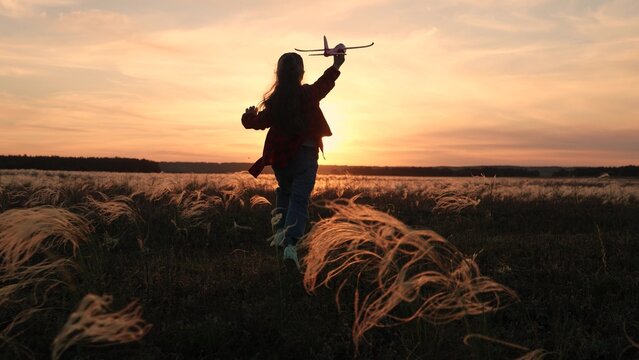 Child girl aviator dreams of fly becoming pilot. Happy kid girl runs with toy airplane on field in sunset sky. Child play toy airplane. Little girl child wants to become pilot astronaut. Slow motion