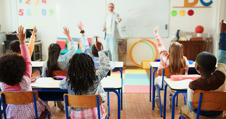 Teacher, students and arms raised in classroom with children for education, question or answer for...