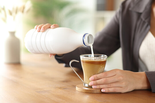 Woman hand pouring milk in coffee mug on wooden table - Powered by Adobe