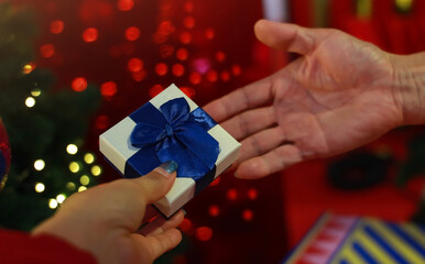 Hand of man giving gift to woman near christmas tree with bokeh background
