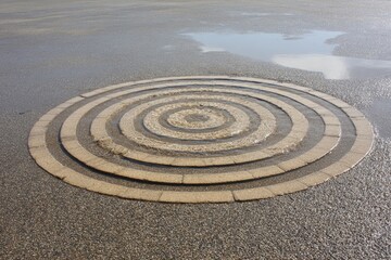 Circular pattern of light beige tiles on dark asphalt, concentric rings, water pooling