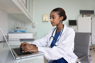 Focused African woman GP in uniform working on laptop