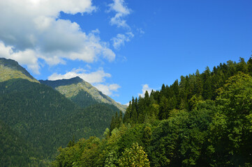 Beautiful mountain landscape. Mountains covered with green trees against blue sky with clouds. Natural background for travel.