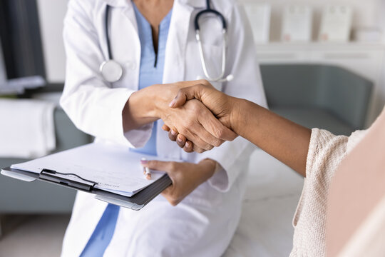 Female doctor holding clipboard and shaking hands with patient