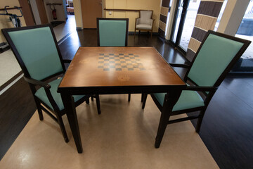 room with a wooden table with a chessboard top wood background surrounded by several chairs arranged around it