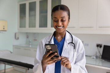 African female doctor in coat using smartphone in clinic office