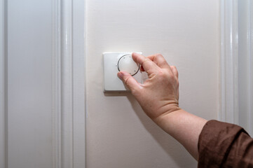 Close-up of a hand turning a wall-mounted thermostat to control home heating. Concept of indoor temperature regulation, energy saving, and heating bills in the United Kingdom