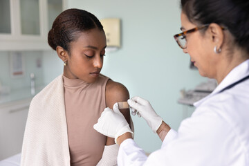 Doctor placing adhesive plaster on shoulder of patient woman