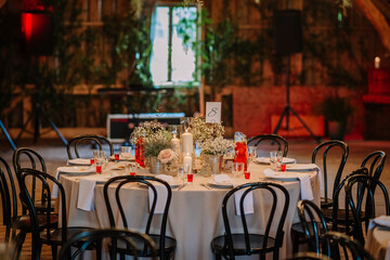 Elegant round table set for a wedding with candles, flowers, and drinks in a rustic indoor venue, featuring a cozy and romantic evening atmosphere.