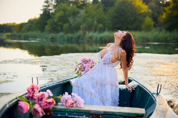 Beautiful woman in white dress on a boat with flowers on a lake in the evening light.