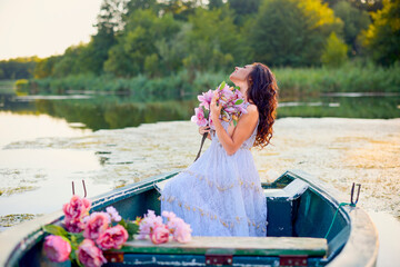 Beautiful woman in white dress on a boat with flowers on a lake in the evening light.