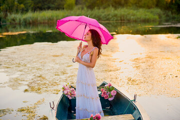 Beautiful woman in white dress on a boat with flowers on a lake in the evening light.