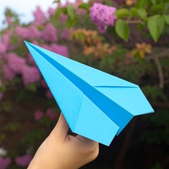 A vibrant blue paper airplane held in a hand against a blurred background of purple flowers.