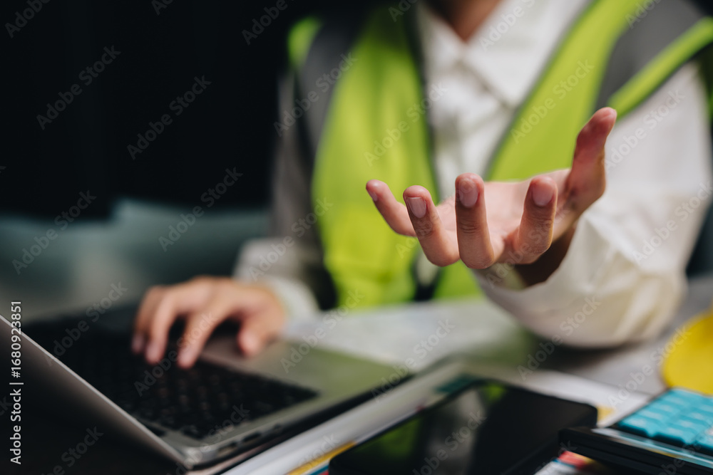 Poster professional engineer discussing project details and working on laptop with papers and smartphone on